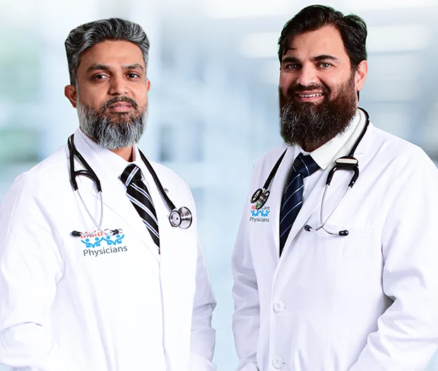 Two professional doctors from Deltona Primary Care Physicians wearing white coats and stethoscopes, standing confidently in a medical office.